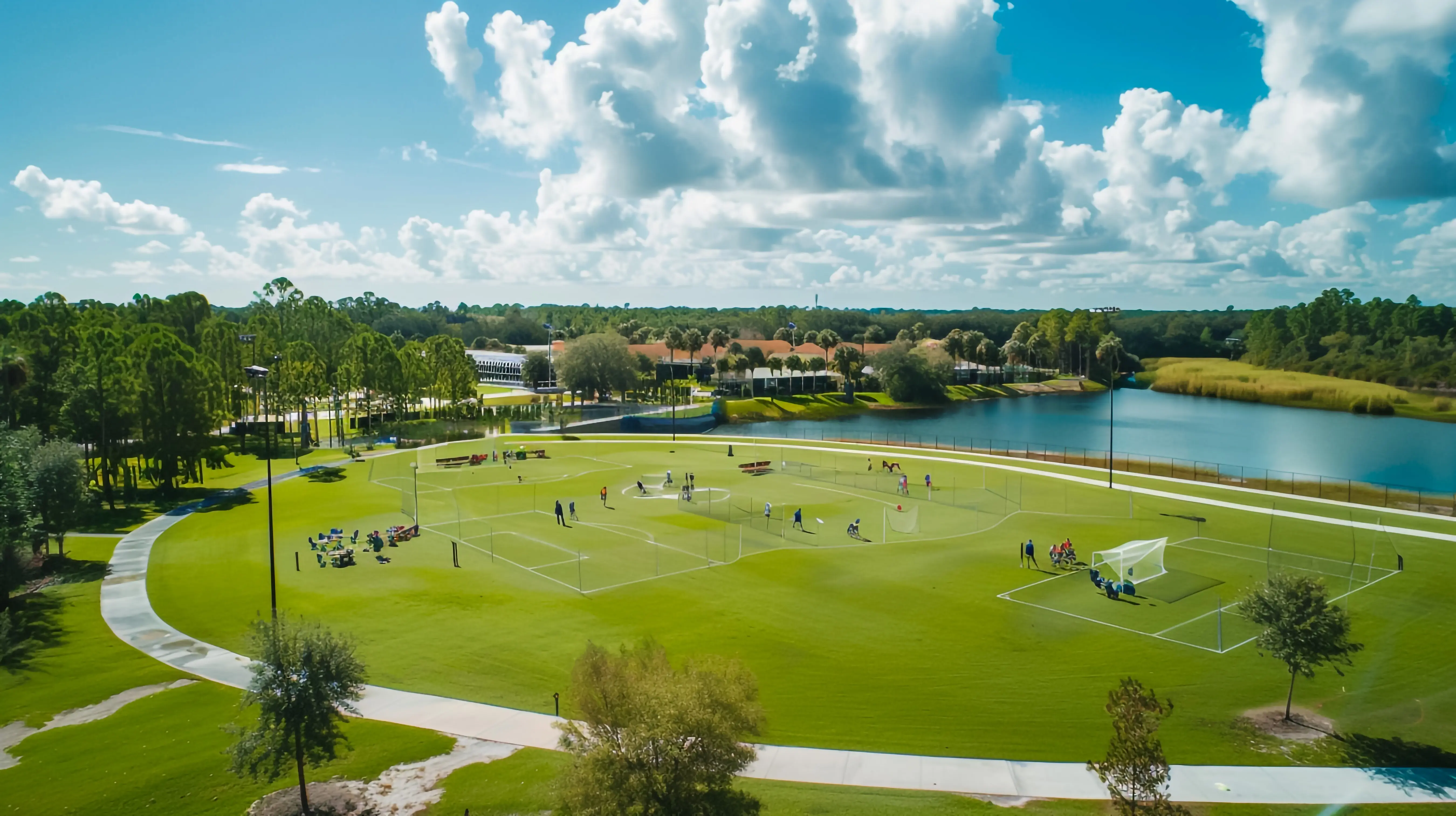 a wide green field featuring a soccer field beneath a blue sky with clouds